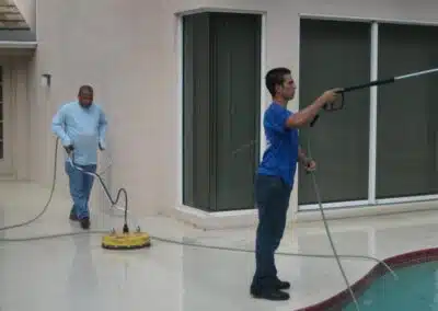 Two men are cleaning a pool with a power washer.