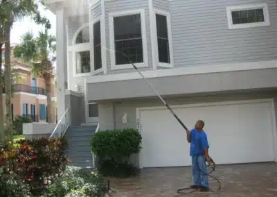 A man in blue shirt holding hose near house.