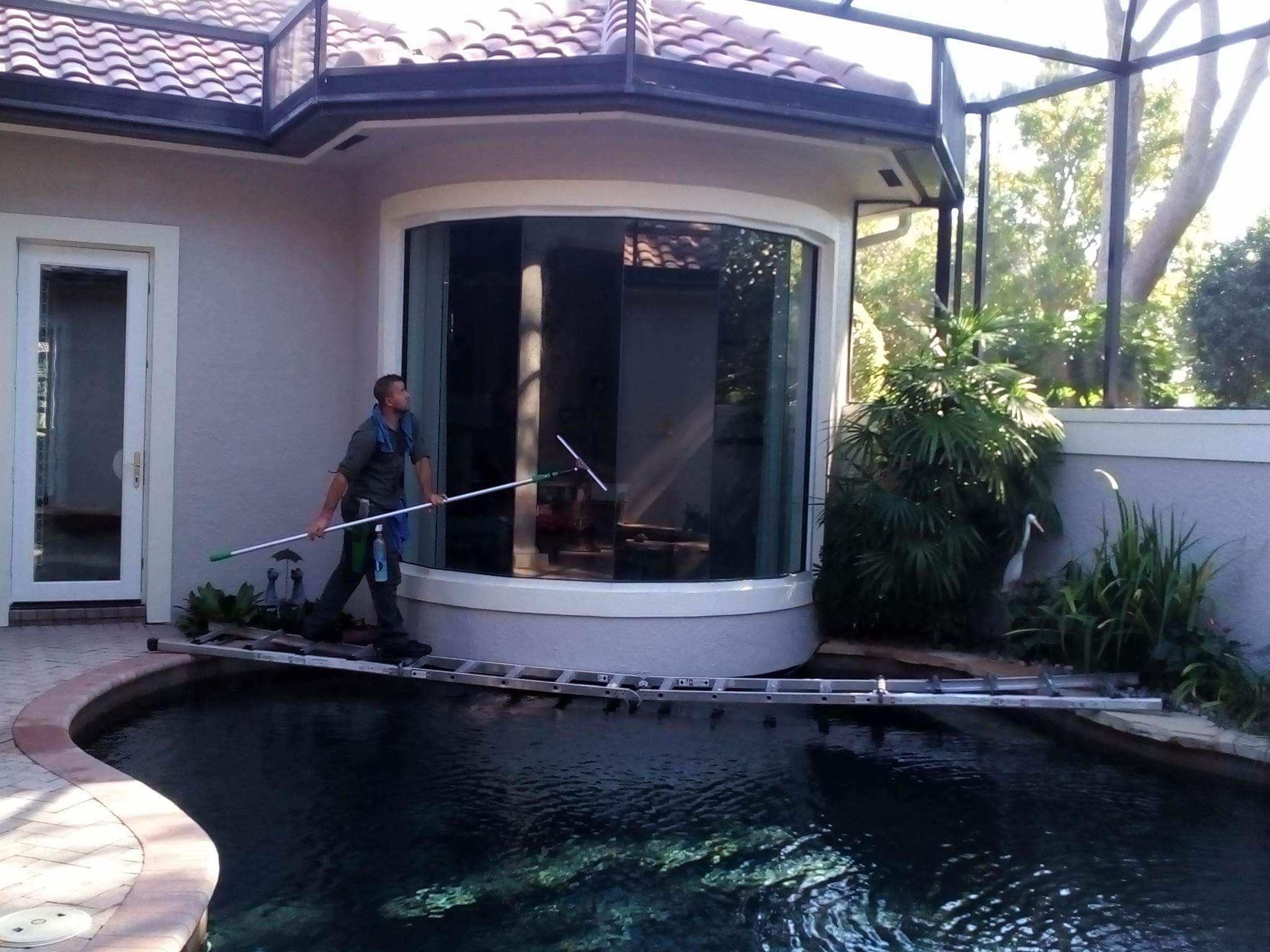 Professional window cleaning service cleaning glass pool enclosure windows at a Naples, Florida home.